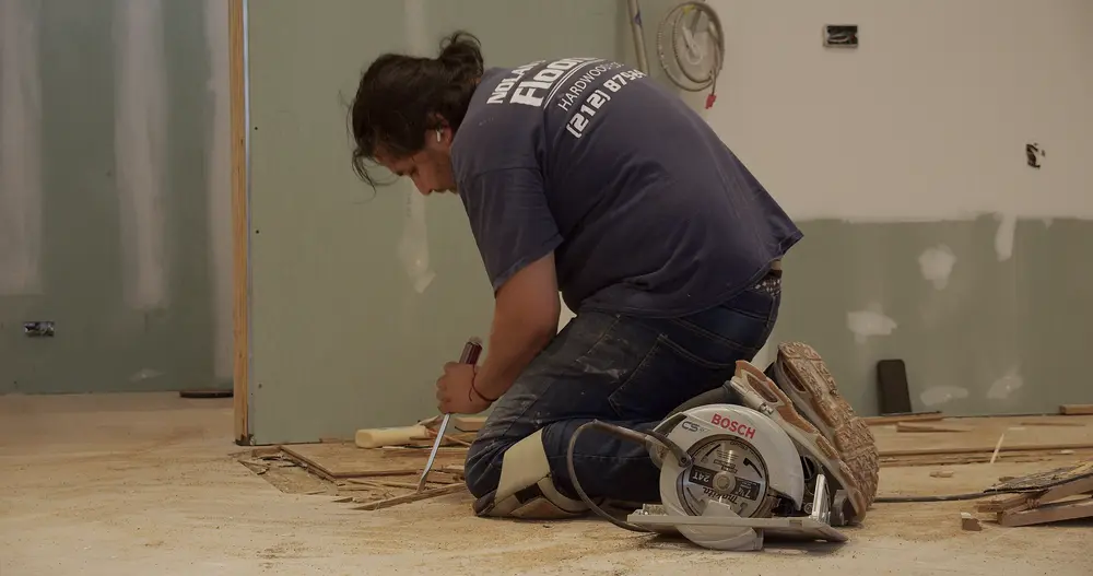 Nolan flooring specialist kneeling to repair a hardwood floor