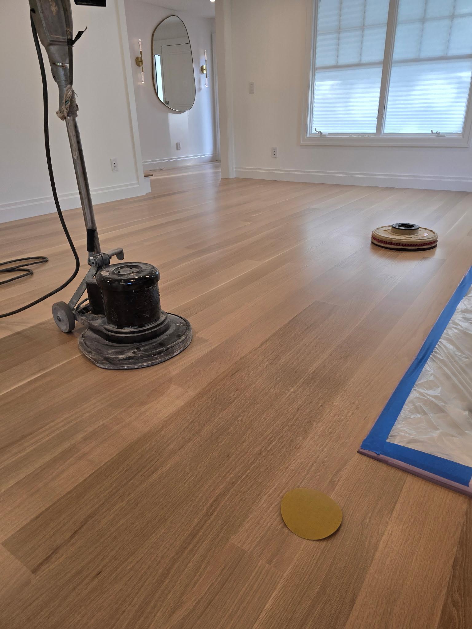 Floor sander and sanding disc on a light hardwood floor during refinishing