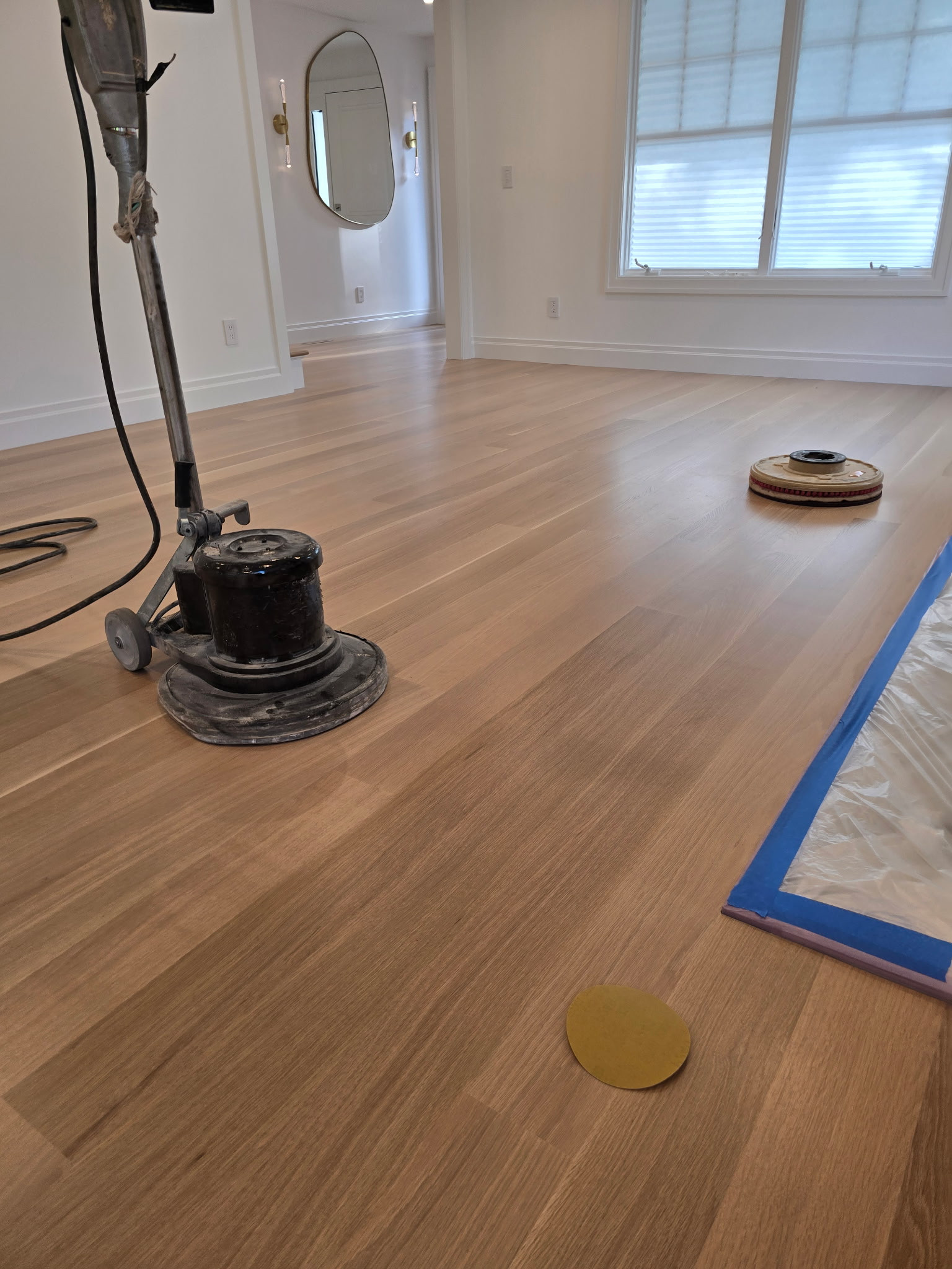 Floor sander and sanding disc on a light hardwood floor during refinishing